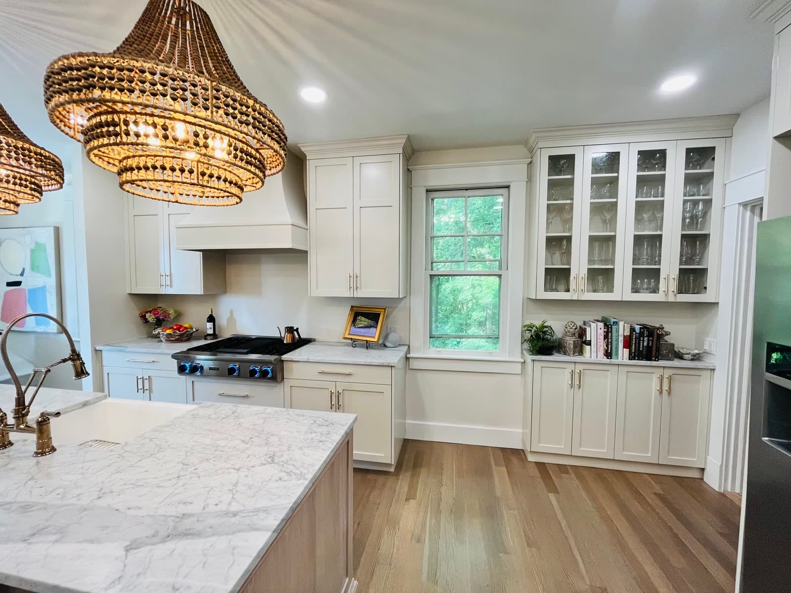 Kitchen remodeled by Yahweh Contractors with glass-front cabinets, window and marble island